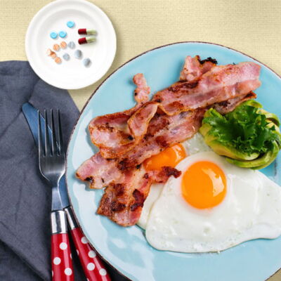 plate of eggs and bacon next to dish of prescription medicines
